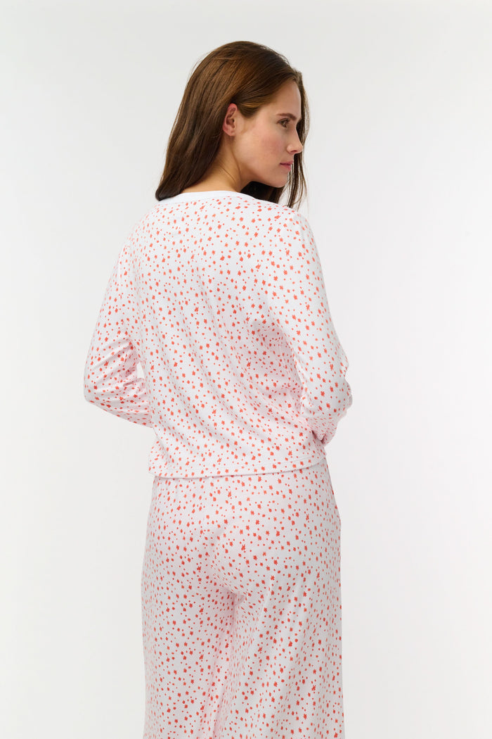 A woman wears the Roller Rabbit Étoiles Nessa Cardigan over a long-sleeve white pajama set with red polka dots, made from cozy Pima cotton in Peru, standing against a light background and looking at the camera with a relaxed expression.