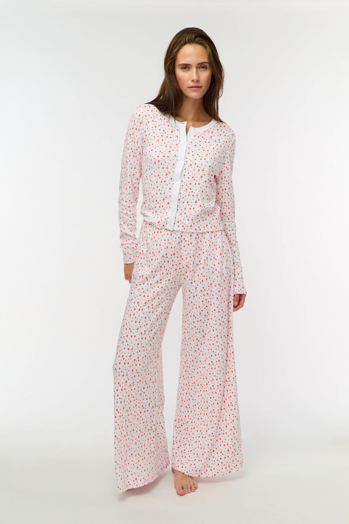 A woman wears the Roller Rabbit Étoiles Nessa Cardigan over a long-sleeve white pajama set with red polka dots, made from cozy Pima cotton in Peru, standing against a light background and looking at the camera with a relaxed expression.